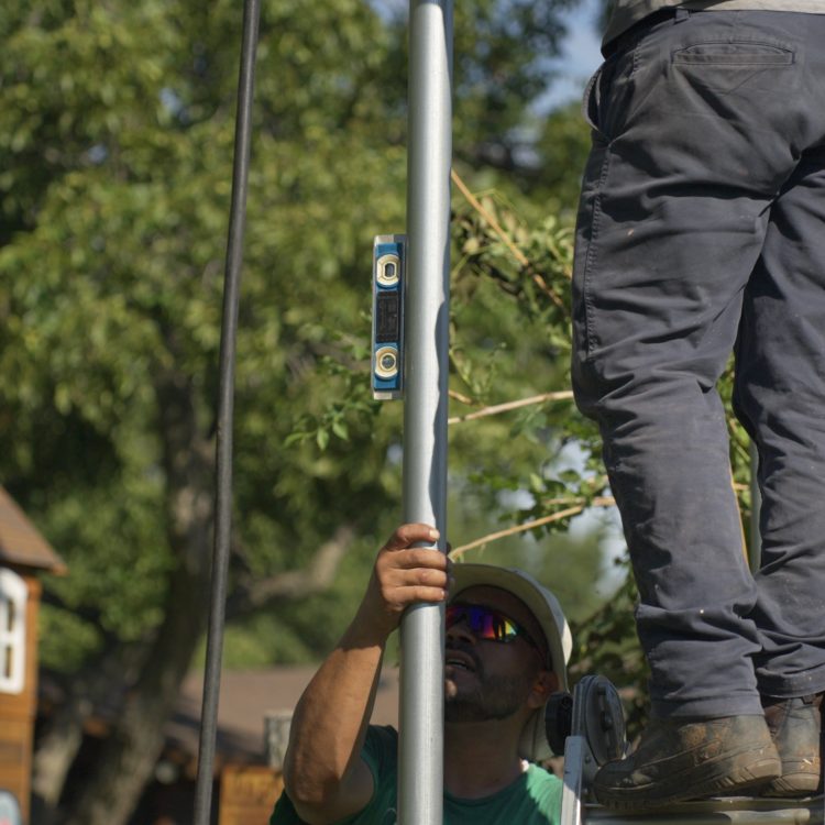Crew leveling steel post, worker in green shirt and another standing