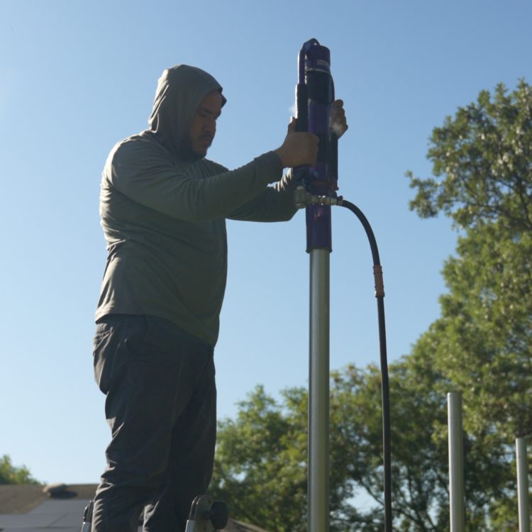 Worker using post driver on steel post against sky