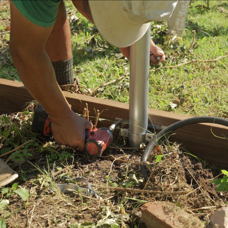 Worker trimming wood rail at base of steel post with grinder